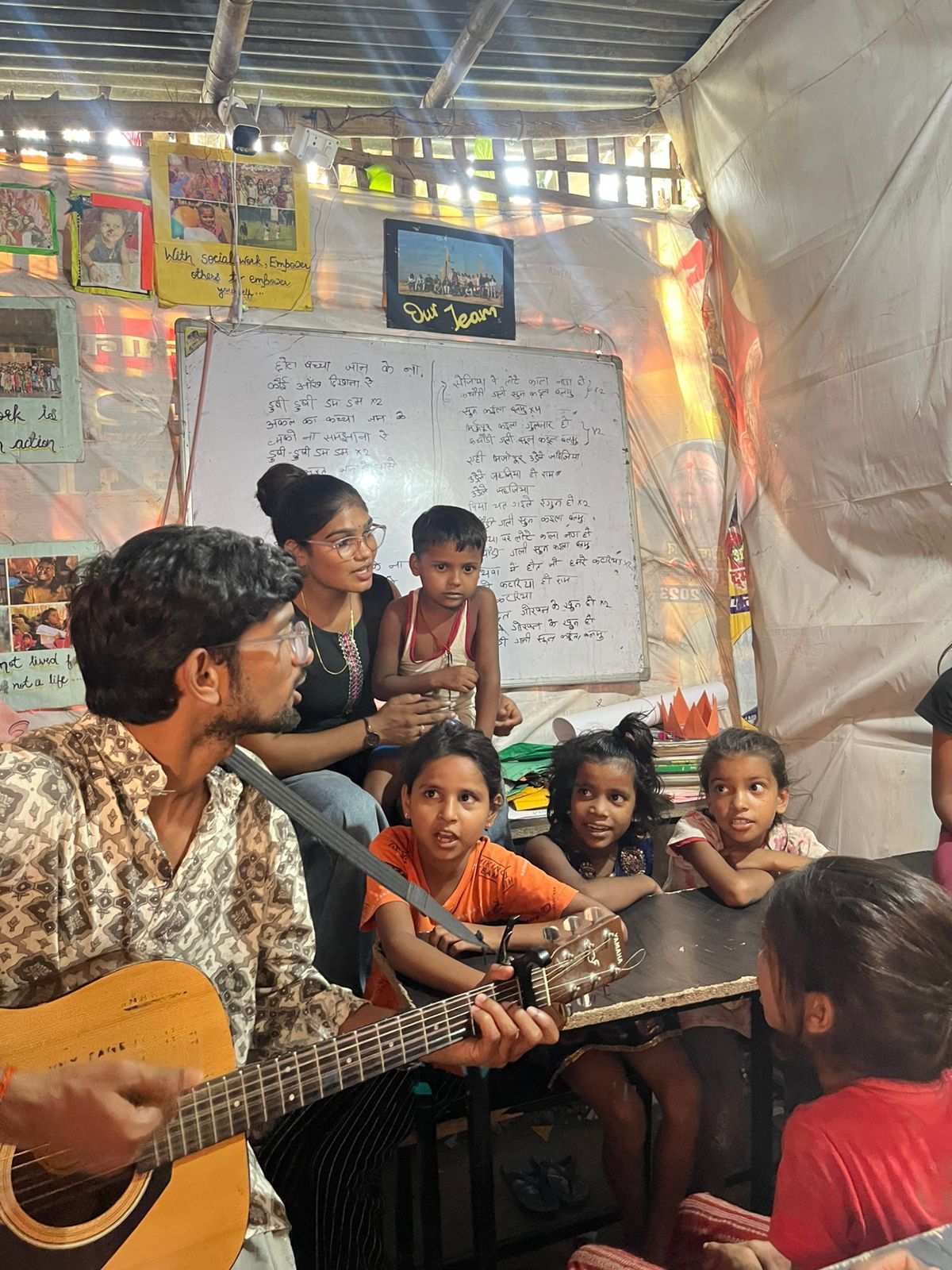 A facilitator playing guitar with young children in a community learning space