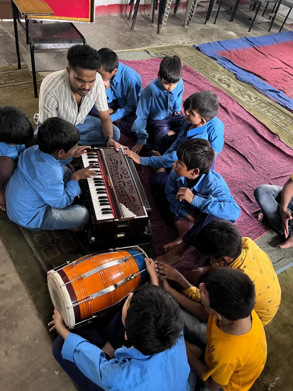 Students seated on the floor around a harmonium and dholak during a music session