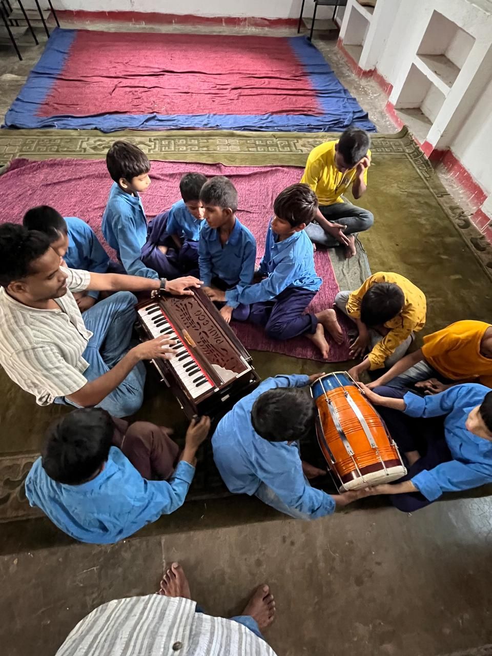 Children gathered closely around a harmonium and dholak, learning by touch and sound